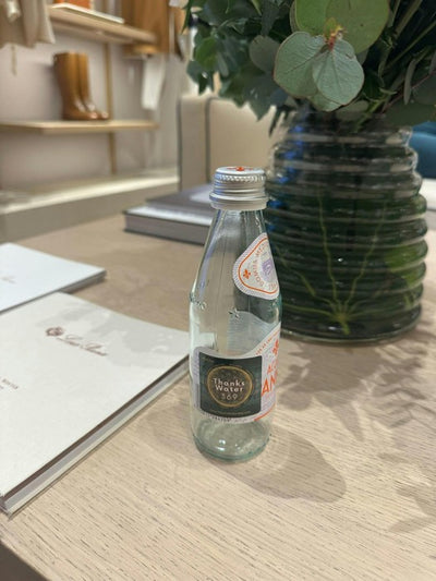 A labelled bottle on a desk beside a notebook and greenery