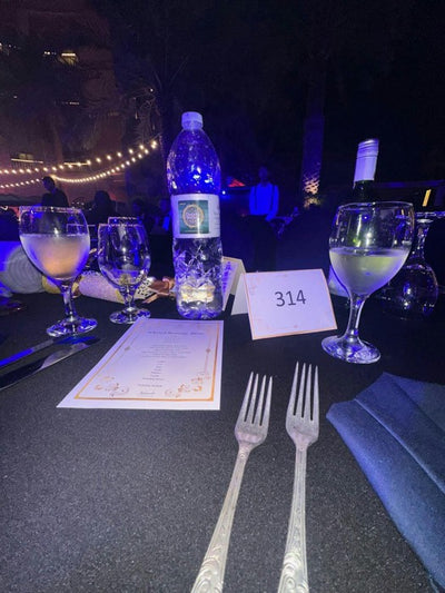 A labelled bottle on a set dinner table in the evening
