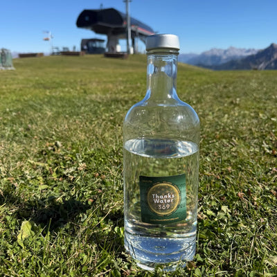 A Health label on a glass water bottle in an alpine meadow below a ski-lift station