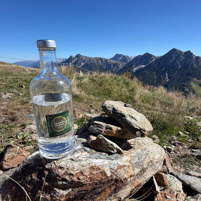 A labelled glass water bottle on a rock with a jagged mountain range behind
