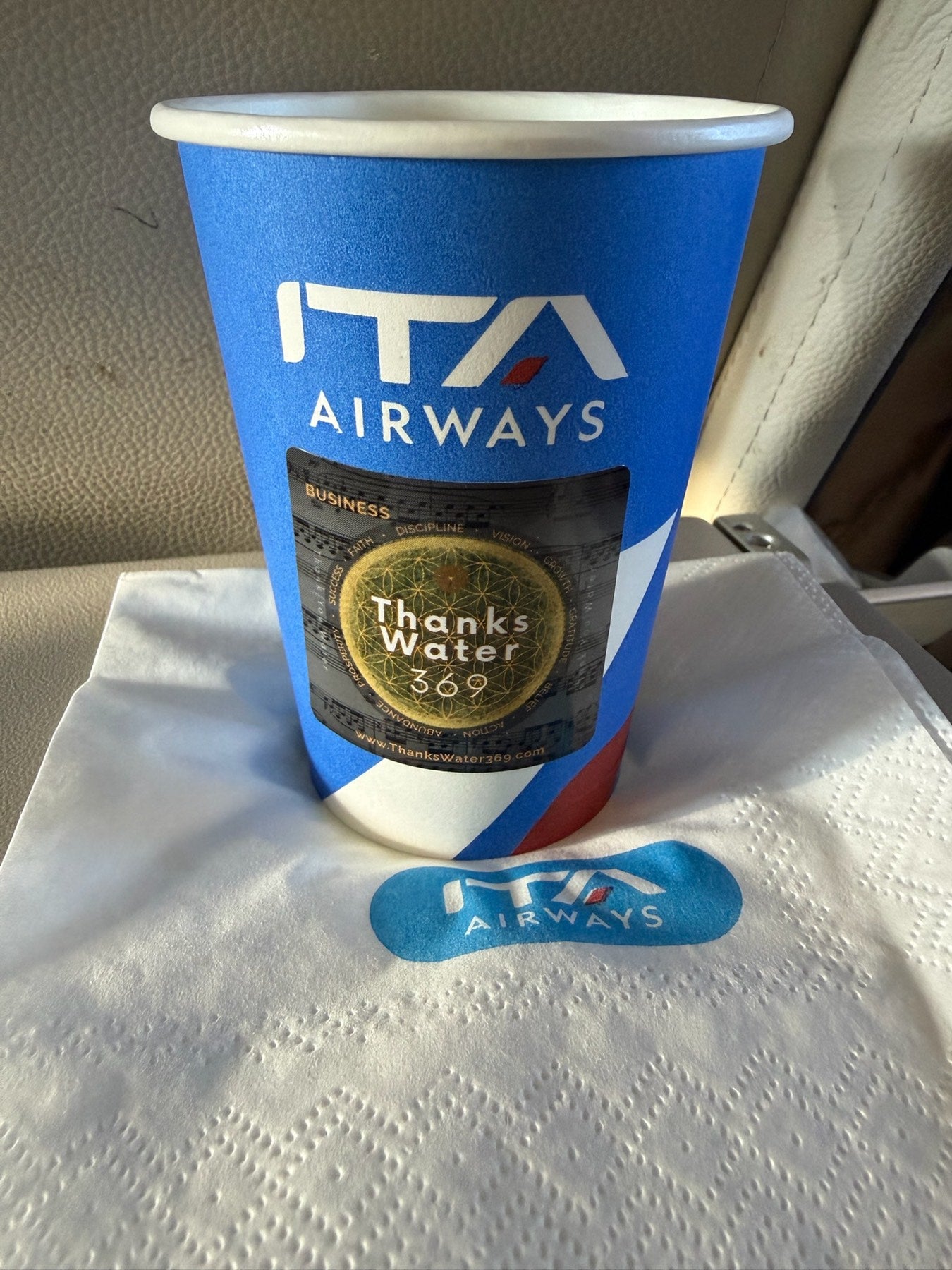 A labelled cup on an aeroplane tray table